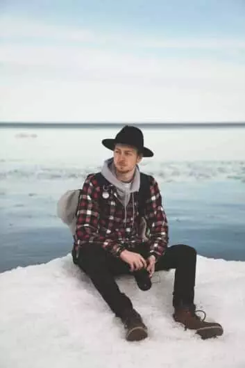 trendy young man resting on snowy hill at seaside